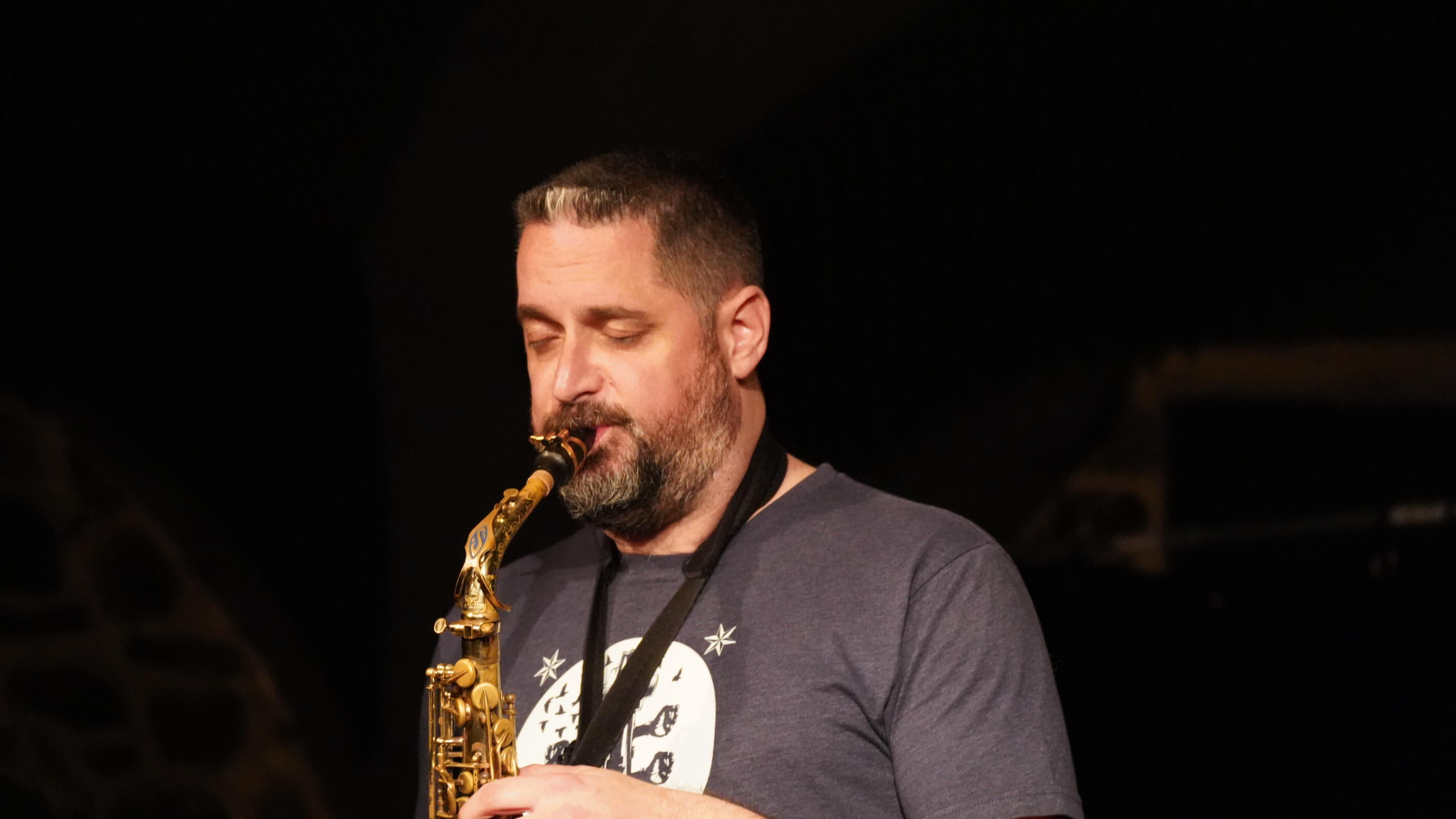 Altsaxophonist im Spotlicht vor dunklem Hintergrund.