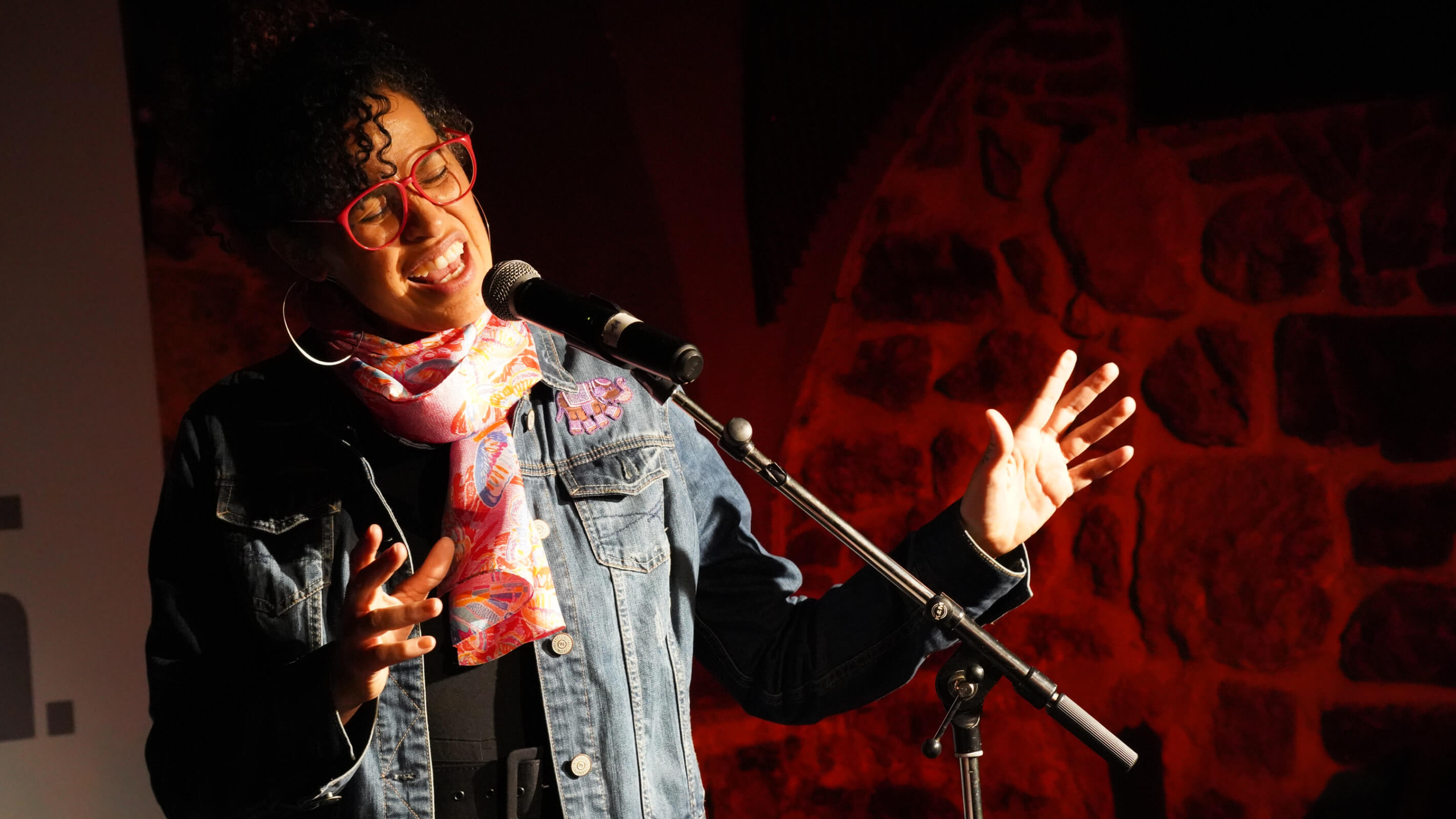 Sängerin am Mikrofon in Jeansjacke und buntem Schal, gestikuliert.