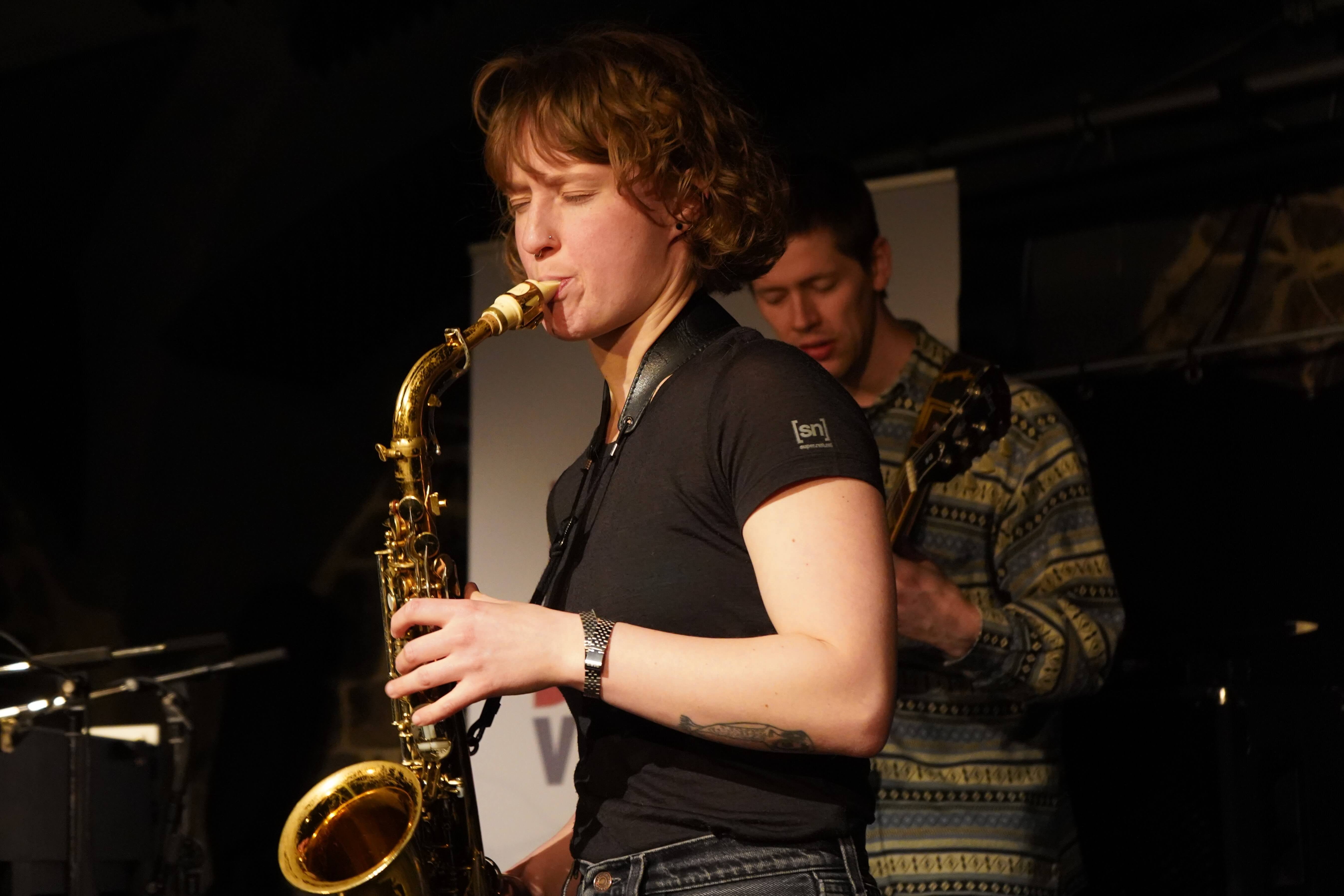 Altsaxophonistin im dunklen T-Shirt, Augen geschlossen, das Horn nach vorn.