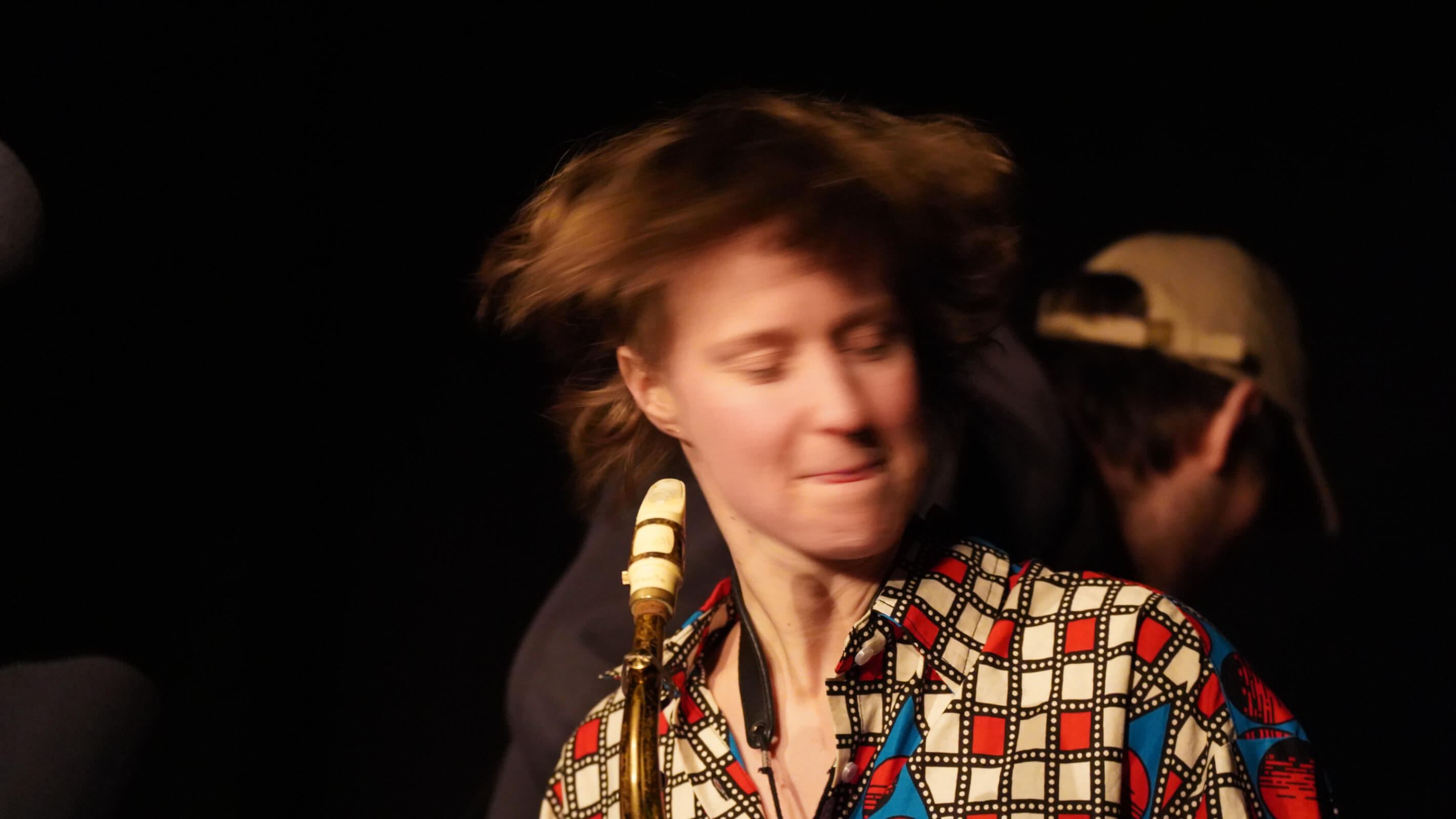 Saxophonistin mit fliegendem Haar in Bewegung, gemustertes Hemd, hartes Licht.