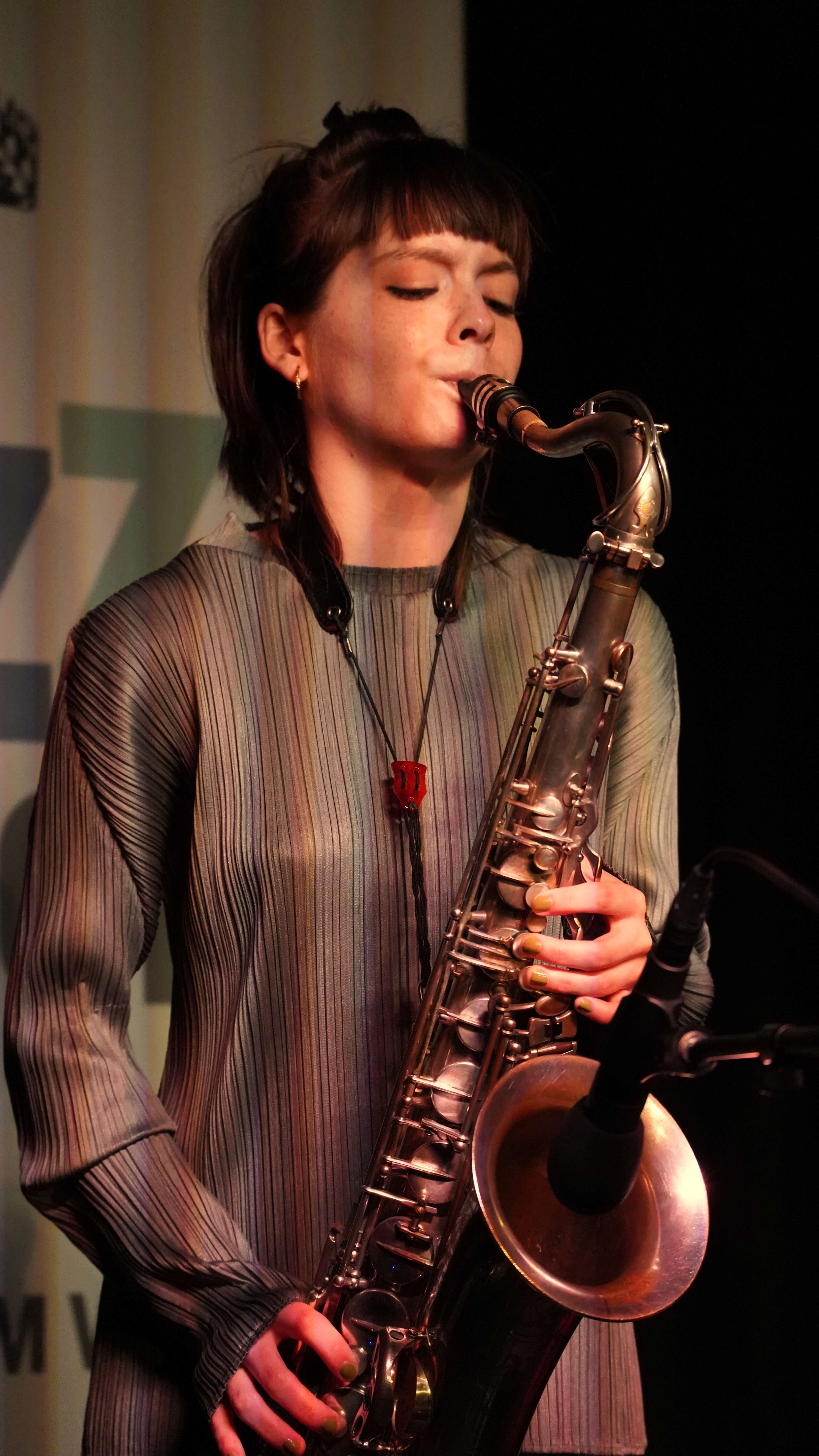 Tenorsaxophonistin im gefalteten Oberteil hält das Horn nah am Mikrofon.