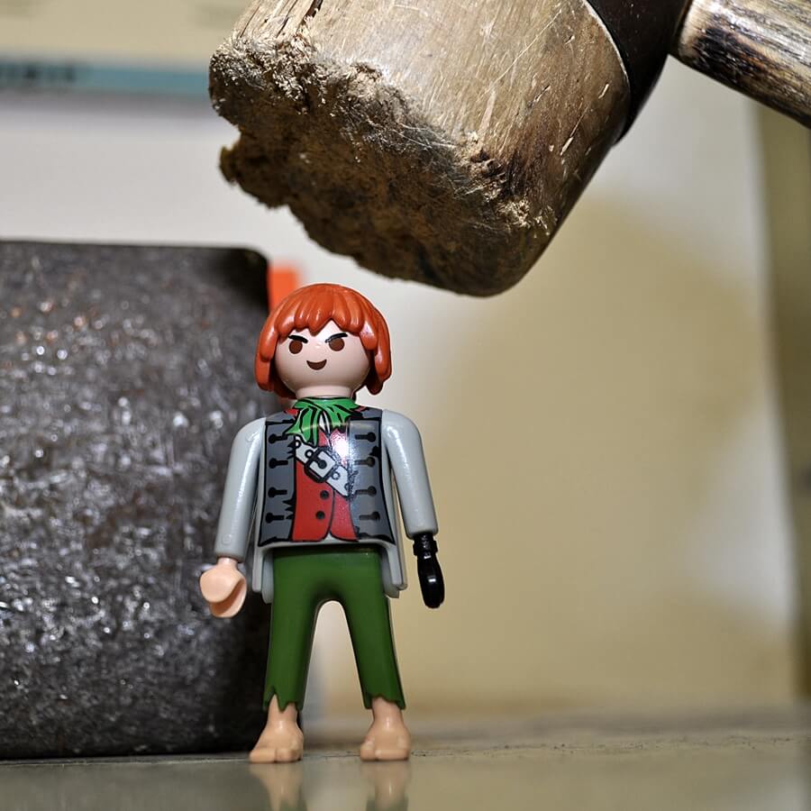 Playmobil-Piratenfigur steht unter einem angehobenen Holzhammerkopf.
