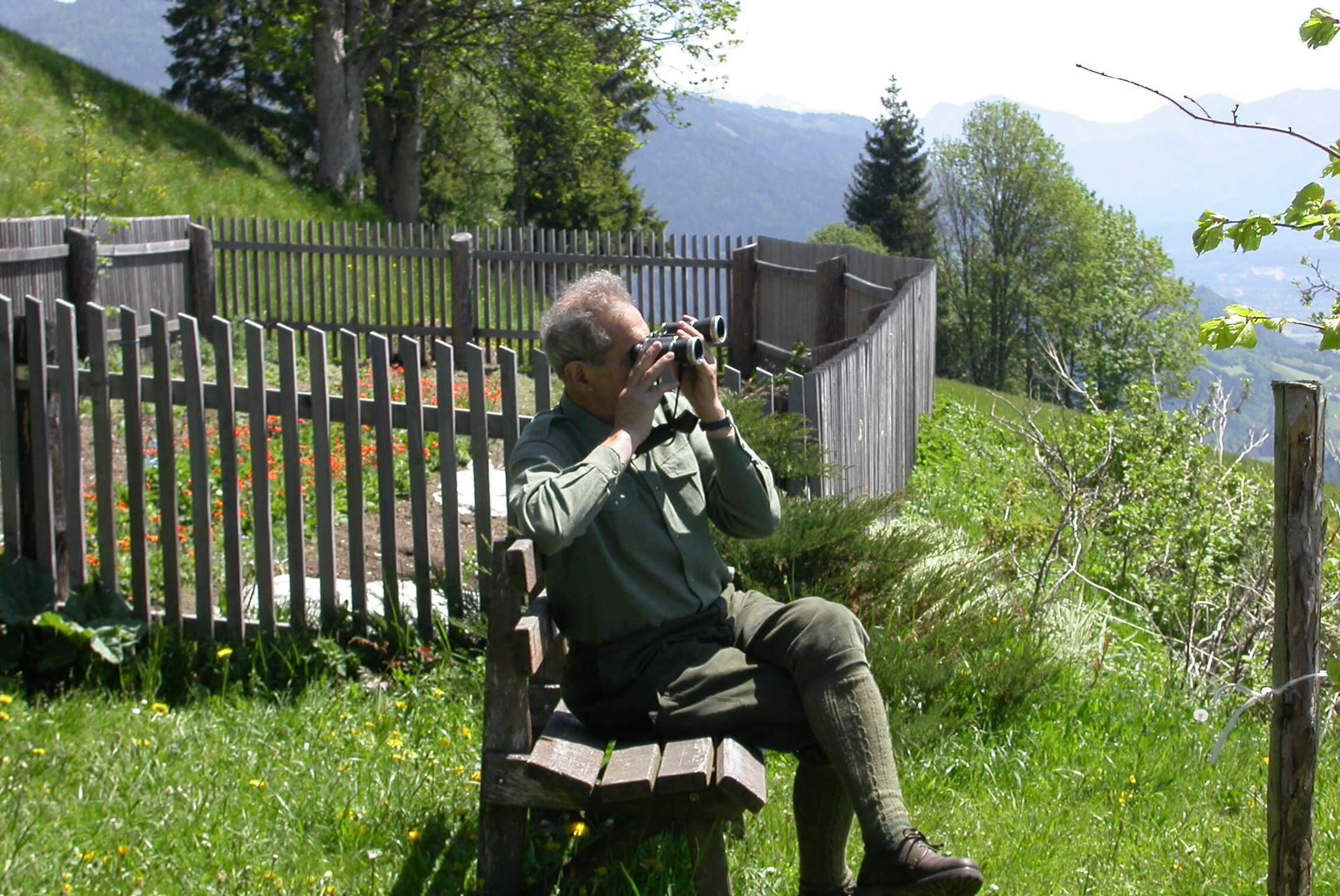Mein Vater, allein auf seiner vertrauten Bank über dem Tal sitzend, die Beine übereinandergeschlagen, das Fernglas erhoben, versunken im fernen Landschaftsraum, den er auswendig kennt.